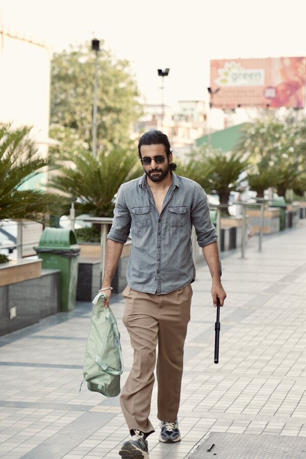 Aman walking down a street at golden hour, sunglasses on, tote bag in hand