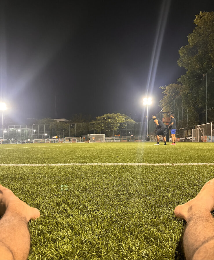 View from the ground of a floodlit turf football pitch at night, teammates mid-game