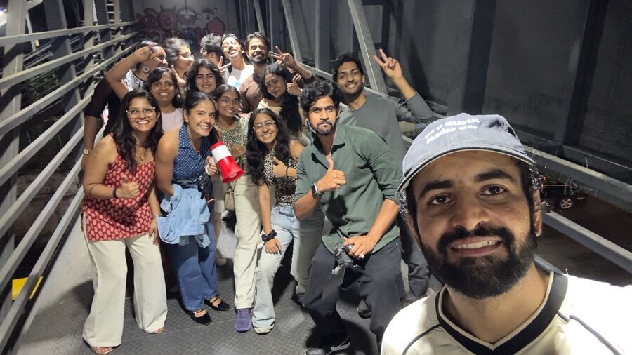 Large group selfie on a steel bridge walkway at night, everyone smiling and posing