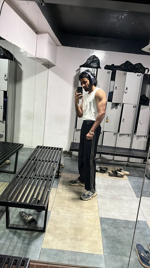 Mirror selfie in a gym locker room, headphones on, mid post-workout check-in